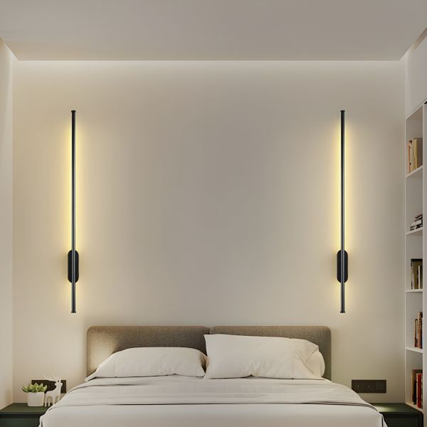 Linear bronze wall light illuminated in a bedroom